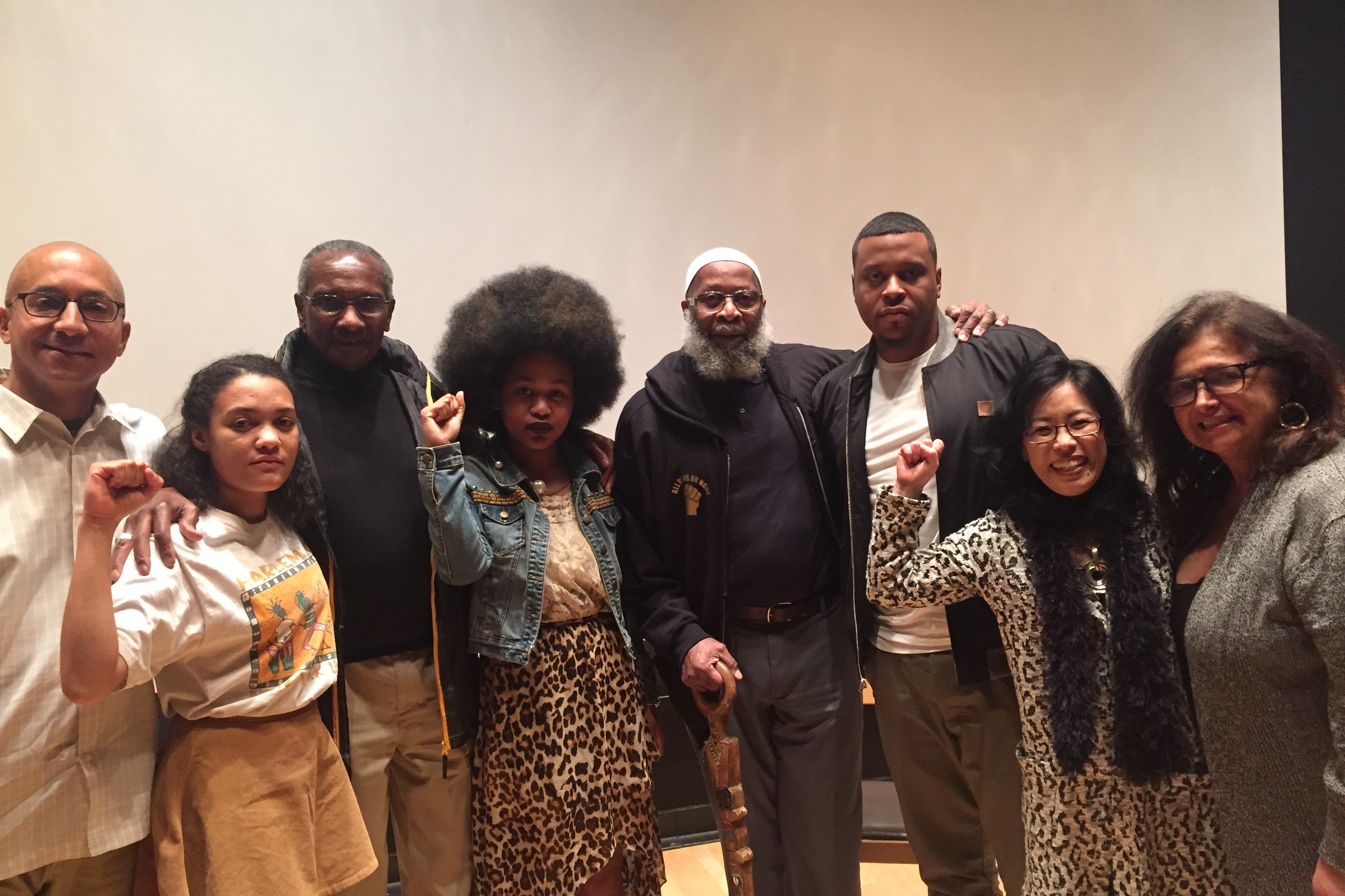 Group of students, professors, and visiting speakers posing with fists raised